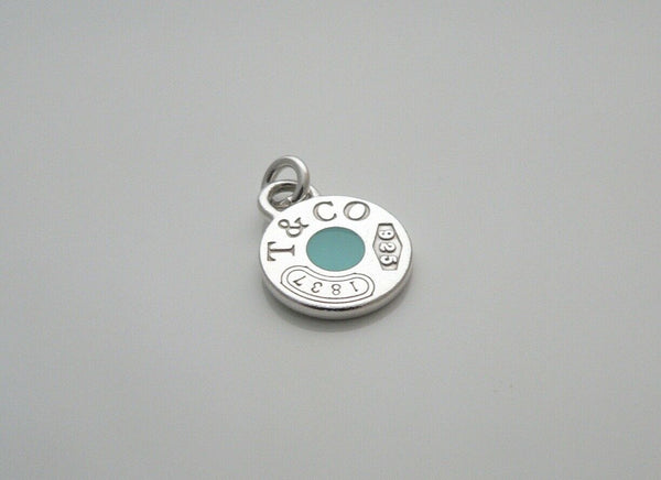 A Tiffany & Co silver charm with a blue enamel circle and the brand's logo in the center.