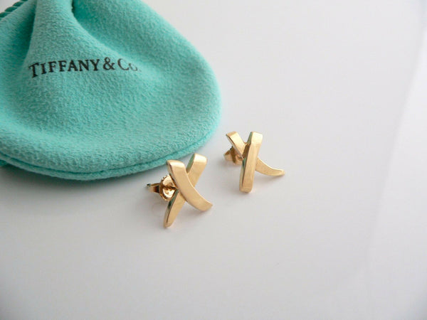 A pair of Tiffany & Co 18K gold medium 'X' kiss earrings, displayed on a blue Tiffany & Co. pouch, against a white background.